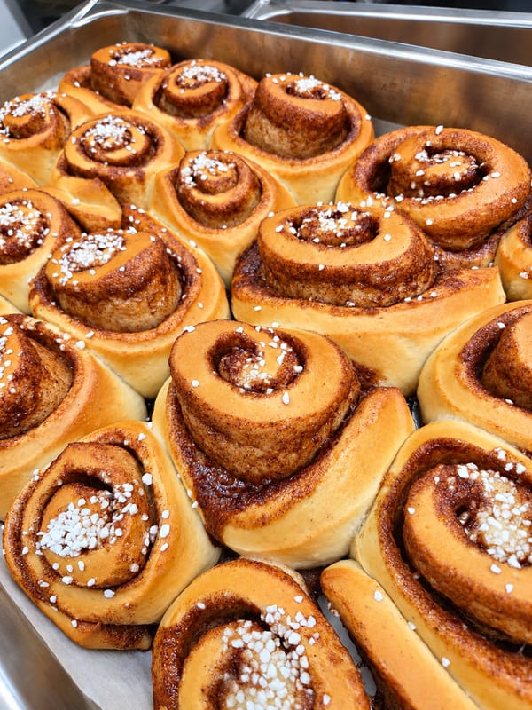 Gyllene kanelbullar med pärlsocker på en bakplåt.